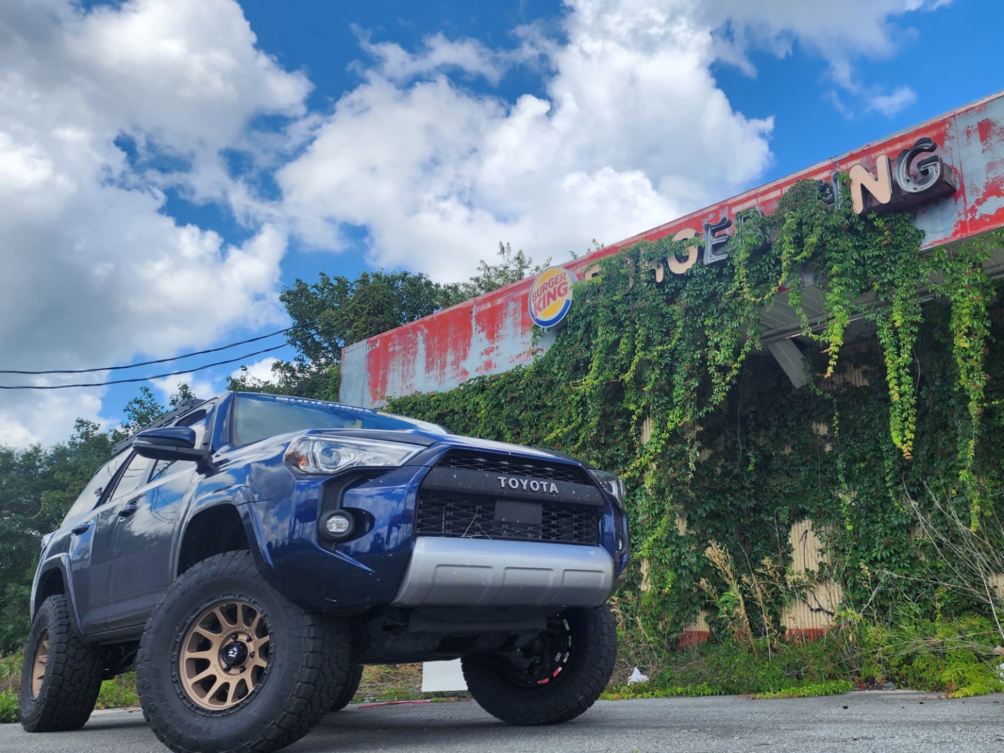 Lifted blue Toyota 4Runner TRD on bronze wheels parked in front of an ivy-covered abandoned Burger King in Florida