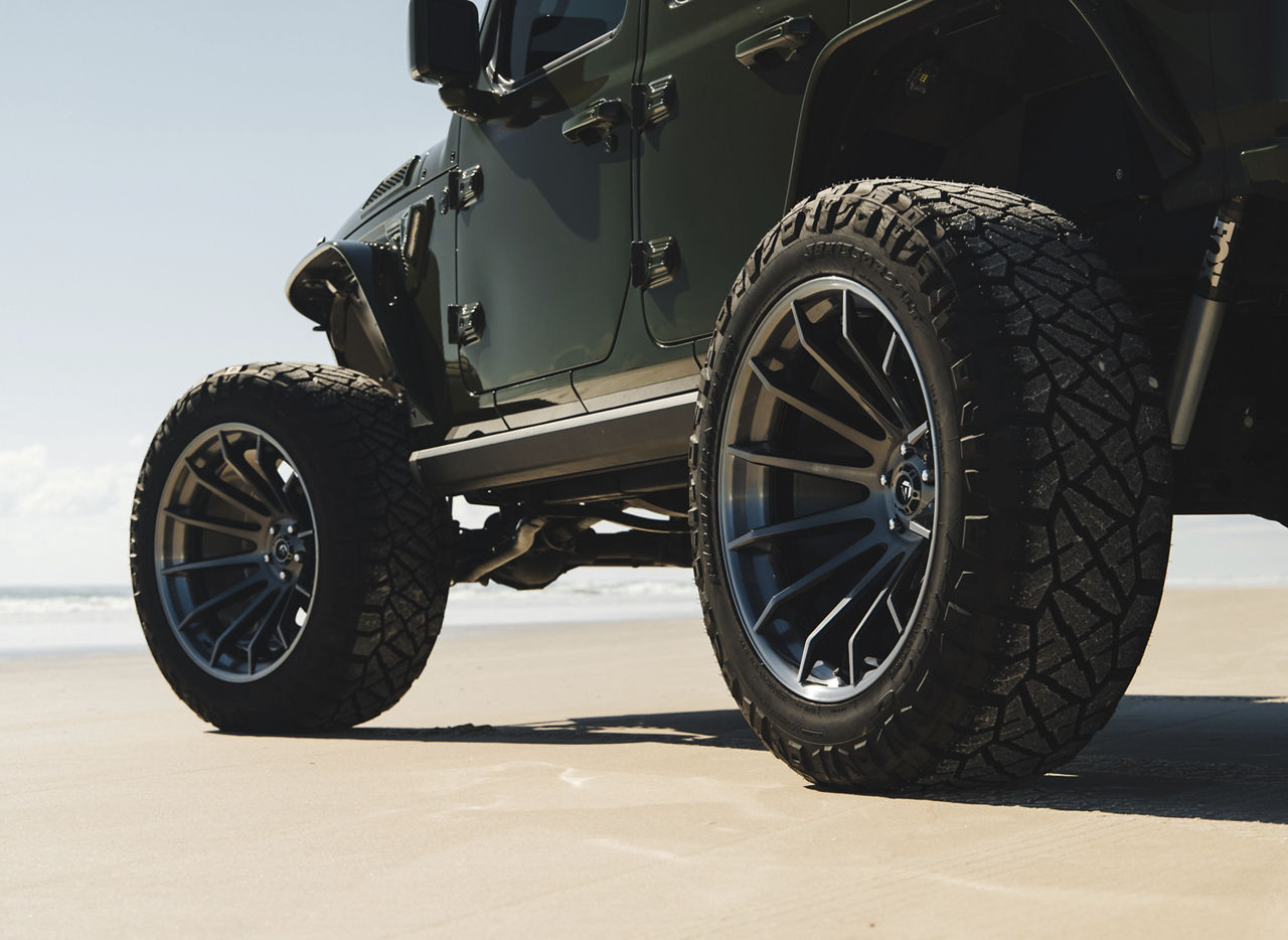 Lifted green Jeep Wrangler with large off-road wheels and all-terrain tires on a sandy beach