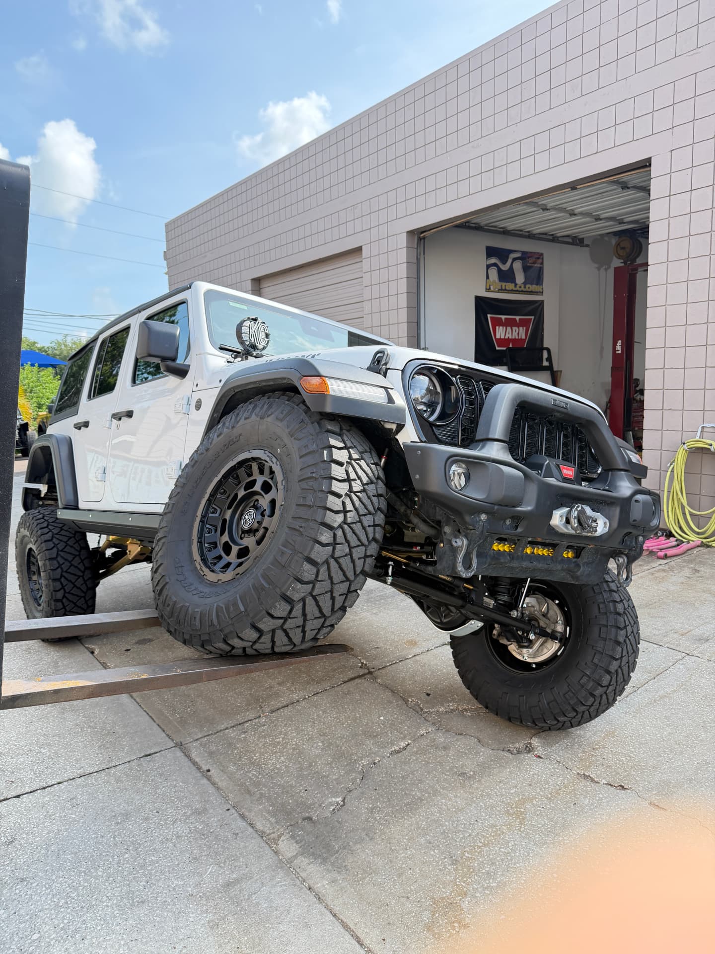 White 2025 Jeep Wrangler JLU Willys with MetalCloak 3.5-inch long arm suspension and Currie HD60 axles, flexing on a ramp with 37-inch Nitto Ridge Grappler tires at SunCoast Off-Road in New Port Richey, FL