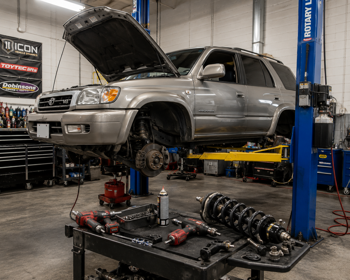 Modified Toyota Tacoma on a two-post lift inside a clean professional 4x4 shop bay